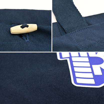 Nahaufnahme von der PEZ Baumwolltragetasche zeigt Details des hellen Holzknebelverschlusses, der robusten Kreuzstich-Naht am Henkel und der Textur des blauen Canvas-Stoffs.